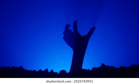 Scary dirty halloween zombie hand silhouette raising up from grave crawling and moving fingers, isolated on blue background. Mystery halloween concept.