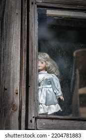 Scary doll looks out the window of an old house. Creepy girl doll in a window