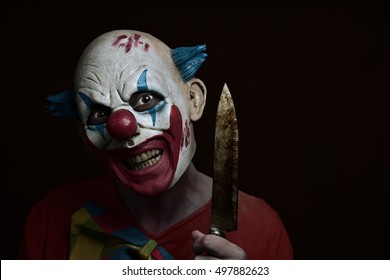 a scary evil clown with a big knife in his hand, against a dark background