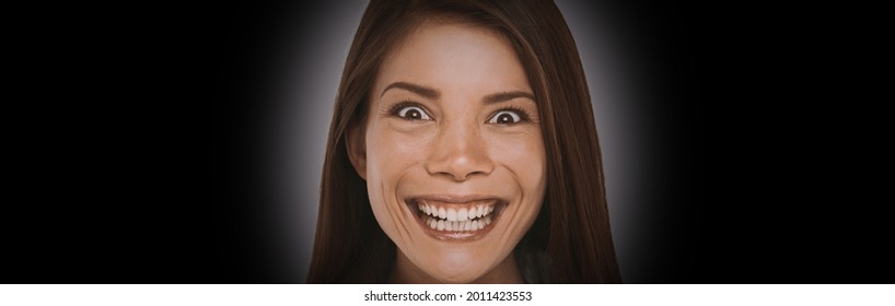 Scary face expression of crazy Asian girl with evil smile on black background banner. Woman smiling with a devilish laugh looking evil.