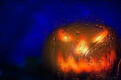 Scary Face Pumpkin Through The Wet Glass With Drops After Rain