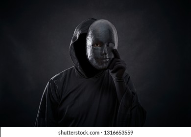 Scary figure in hooded cloak with mask in hand 