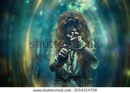 Scary forest witch with a mask covering her eyes in a dark gloomy forest creating a magic portal. Woman shaman. Paganism. Death ritual. Halloween. 