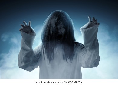 Scary ghost woman with blood and angry face with clawing hands standing amid the dark fog. Halloween concept