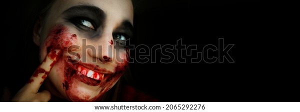 Scary girl in the
image of a zombie.
Halloween theme portrait of crazy girl with
bloody face. Zombie theme, black background, isolated, killer.
Banner, copy of the space.
