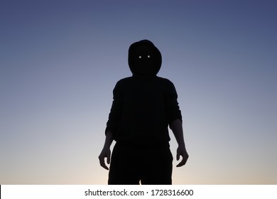 A scary, hooded figure with glowing evil eyes and blank black space where his face should be looking down to camera                      