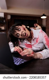 Scary Horrific Zombie Using Laptop At Desk, Undead Corpse Trying To Work On Computer In Startup Office. Creepy Aggressive Brain Eating Monster Looking Terrifying And Horrible, Sinister Danger.