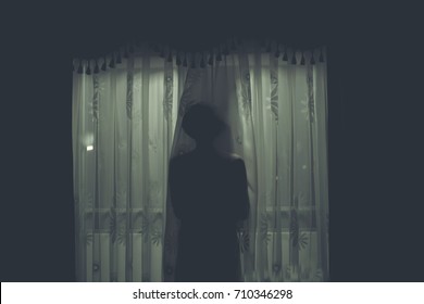 Scary human body silhouette woman front of window behind the black curtain.