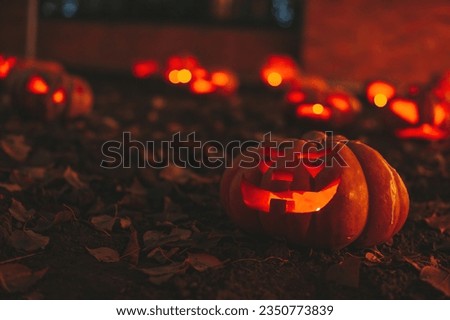 Scary jack lantern halloween pumpkins in darkness on ground among dry leaves at street. Hallows eve decoration funny glow pumpkin with candles on dark background in open air near house