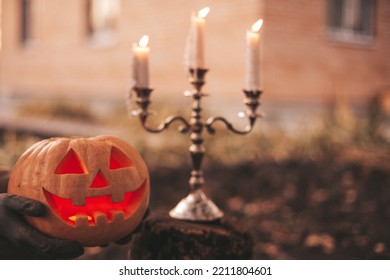 Scary Jack O Lantern Halloween Pumpkins In Sun Day On Ground Among Dry Leaves At Street. Hallows Eve Decoration Funny Glow Pumpkin With Candles On Candlestick At Fall Background In Open Air Near House