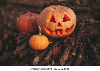 Scary Jack O Lantern Halloween Pumpkins In Sun Day On Ground Among Dry Leaves At Street. Hallows Eve Decoration Funny Glow Pumpkin With Candles On Candlestick At Fall Background In Open Air Near House