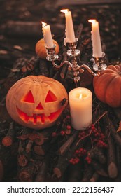 Scary Jack O Lantern Halloween Pumpkins In Sun Day On Ground Among Dry Leaves At Street. Hallows Eve Decoration Funny Glow Pumpkin With Candles On Candlestick At Fall Background In Open Air Near House