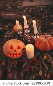 Scary Jack O Lantern Halloween Pumpkins In Sun Day On Ground Among Dry Leaves At Street. Hallows Eve Decoration Funny Glow Pumpkin With Candles On Candlestick At Fall Background In Open Air Near House