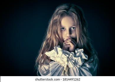 Scary little girl ghost in a white nightgown folded her hands in prayer. Black background. Halloween. 