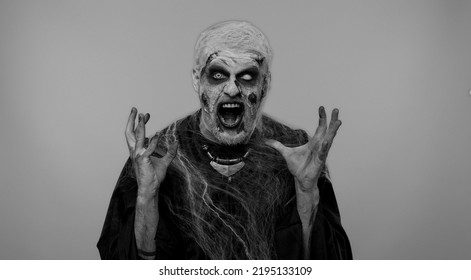 Scary Man In Carnival Costume Of Halloween Crazy Zombie With Bloody Wounded Scars Face Screaming, Shouting, Trying To Scare On Gray. Horror Theme Of Cosplay Wounded Undead, Beast, Monster