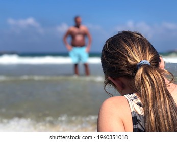 Scary Man watching a young girl on the beach. Child sitting alone on the beach of Tel Aviv, Israel. Over the shoulder of a young lady sitting on the shore with a harassing dark Man in the background.