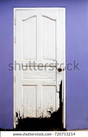 Scary old broken wooden white door and purple color wall. Concept for dirty, destroyed, abandoned.