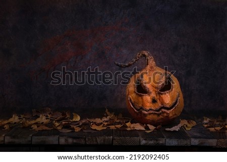 Scary pumpkin lantern with an evil Halloween grin, on a dark blue background on wooden boards, autumn leaves. copy space. Horror.
