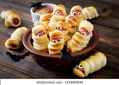 Scary sausage mummies in dough with funny eyes on table. Funny decoration. Halloween food.