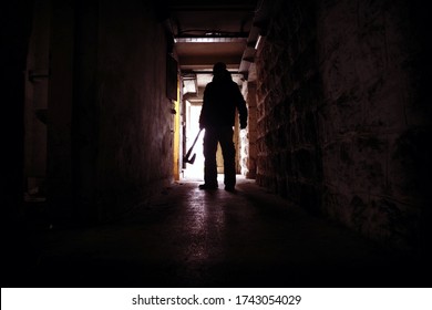 Scary Traumatic Scene. Silhouette Of A Man Holding An Ax In A Dark And Creepy Hallway