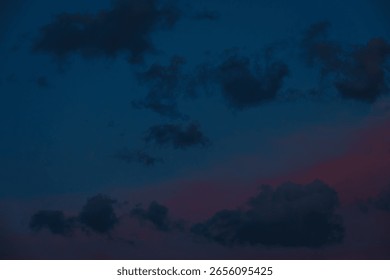 Scattered dark clouds float across a twilight sky bathed in deep blue and delicate pink tones, creating a peaceful and moody scene with copy space.
