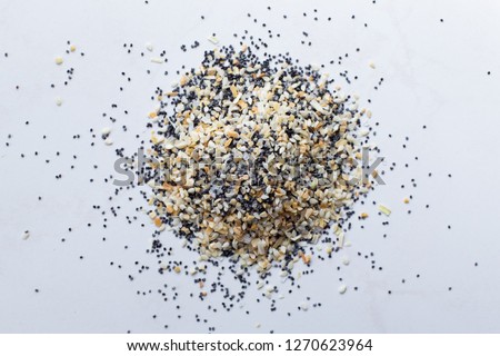 A scattered pile of Everything seasoning containing dried garlic, onion, poppy seeds, sesame seeds and salt on a white background. 