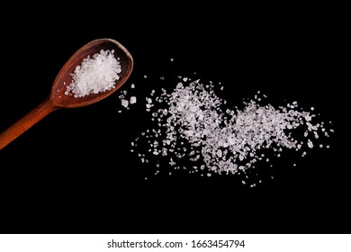 Scattered salt crystals on a black background. Wooden spoon with salt close-up.