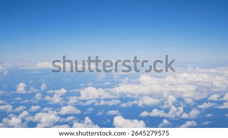Scattered small white clouds seen from above through an airplane window. Bright blue sky and peaceful aerial atmosphere.