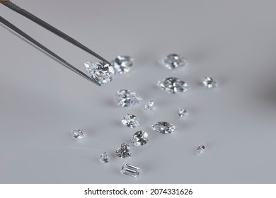 Scattering of gem stones of different cuts and sizes, in focus Pear cut diamond in tweezers on white background.