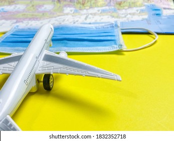 Scenario Of Air Travel During The COVID-19 Outbreak. A Close-up Of A Simulated Plane With A Medical Mask And Blurred Paper Map. Concepts Of The Impact On The Air Transportation Business