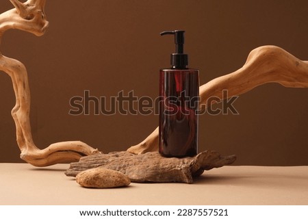 Scene with amber bottle without label and dried twigs decorated on brown background. Blank plastic cosmetics container for cream, lotion or shampoo. Blank minimal design concept