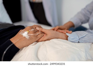 scene of bedridden patient, focus on hand of illness's relative holding hands elderly hopeless senior male with infectious disease, concept of nursing home care or medical treatment in hospital ward - Powered by Shutterstock