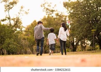 Scene From Behind Of Asian Happy Family Spend Time Together Walking And Relaxing At The Park In The Afternoon Autumn, Concept Family Togetherness, Warm Hearted Family, Parenthood, Happy Family Outing.