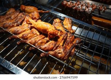 The scene captures a tantalizing array of grilled chicken wings sizzling on a metal rack, showcasing their rich, golden-brown color and crispy texture. The wings are perfectly cooked, glistening with a savory glaze that hints at a blend of spices and marinades typical of Asian street food. In the background, a variety of skewered meats can be seen, adding to the vibrant atmosphere of a bustling night food market in China.