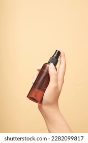 Scene of female hand holding an empty plastic bottle with no label preparing to spray on beige background. Advertising photo for cosmetic product, front view, copy space.