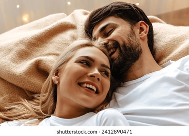 In a scene of love and joy, a young couple lies together on a bed, laughing heartily. Their shared emotions and fun are palpable in this cozy, intimate moment, symbolizing deep affection - Powered by Shutterstock