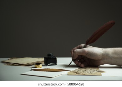 Scene With A Man's Hand Writing A Letter Or Story With Vintage Quill And Old Pieces Of Paper On White Table - With Copy Space For Text