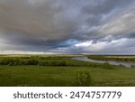  scene of a meandering river cutting through a vast floodplain. The contrast between the stormy sky and the lush greenery creates a dramatic and serene atmosphere. 