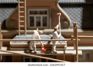 A scene of miniature figures, workers on wooden scaffolding painting and repairing the facade of the building. - Powered by Shutterstock