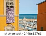 A scene from the old town of Menton: a sheet hanging from the window and a view of the marina with the lighthouse. Provence, France