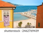 A scene from the old town of Menton: a sheet hanging from the window and a view of the marina with the lighthouse. Provence, France