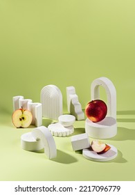 A Scene With A Red Apple With A Composition Of White Podiums Of Different Sizes And Shapes On A Green Background And A Shadow From Sunlight. Stand For Demonstration Of Models