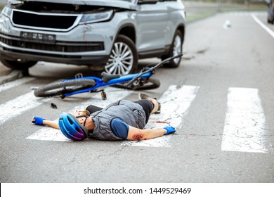 Scene of a road accident with injured cyclist lying on the pedestrian crossing near the broken bicycle and car