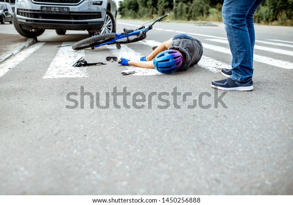 Scene of a road\
accident with injured cyclist lying on the pedestrian crossing near\
the broken bicycle and\
car