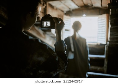 Scene showing photographer capturing silhouette of woman near open window with beams of light streaming in, highlighting rustic wooden interior. Photographer is holding camera - Powered by Shutterstock