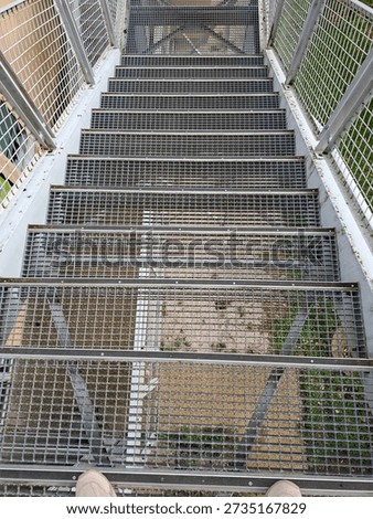 The scene shows a view down a long mesh staircase from a walkway that crosses over a busy highway. The metal stairs are clearly visible with a view of the ground below.