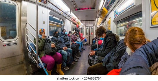 The scene in a subway train wagon, daytime passengers in mask seats on a bench and looking to the phone, super wide-angle panorama view, New York, Bronx, United States of America, 12.22.2021