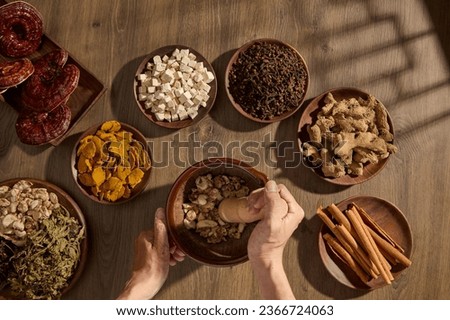 Scene of traditional medicines on wooden trays, decorated on vintage table background with window shadow. Top view, the apothecary's hand is pounding medicine in a wooden mortar