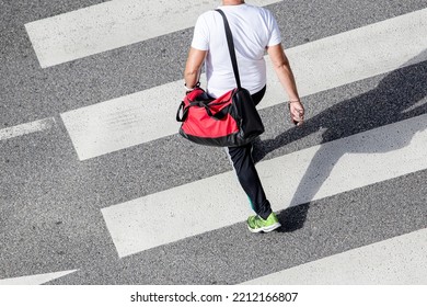 Scene Of A Unrecognizable Man Wearing Sportswear And Carrying A Gym Bag Walking On A Zebra Crossing On His Way To A Sports Center. High Angle View