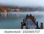 Scenery of beautiful Lake Chuzenji on a foggy autumn evening, with wooden piers extending onto the misty water and lakeside hotels surrounded by colorful foliage in Nikko National Park, Tochigi, Japan